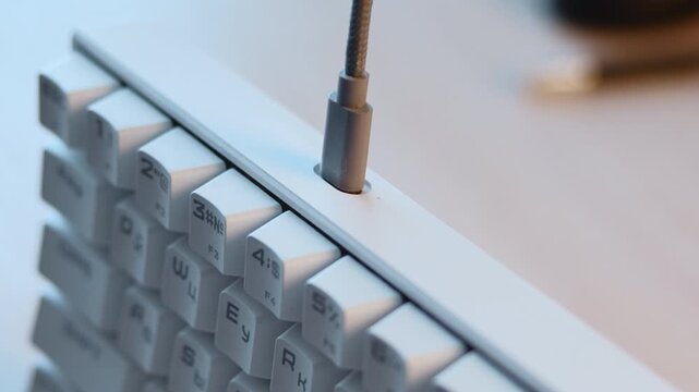 Close-up cable plug connecting into recessed port on white keyboard, showing precise insertion, shallow depth focus, clean workspace details and modern computer interaction