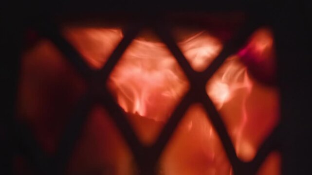 Glowing orange-red flames behind dark diamond metal grate, with shifting bright cores, curling tendrils, vivid heat, soft shadows, and intense contrast creating warm atmospheric motion