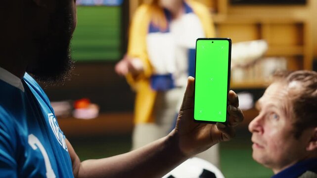 Chroma key phone used by happy football fans having fun with beer and popcorn as joyous soccer supporters follow game broadcast on isolated screen smartphone.