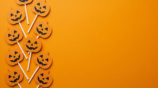 Halloween orange background featuring jack-o'-lantern lollipop paper cut out left border, copy space for spooky party invitation, greeting card, banner, poster, flyer and festive autumn design