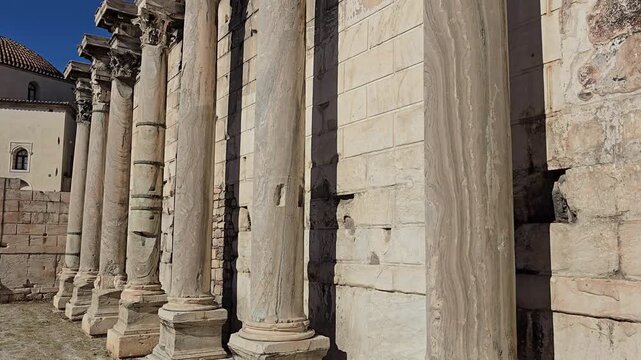 Athens, Greece - 22 June 2026. Low angle view along the western fa&ccedil;ade of Hadrian's Library with Corinthian columns, carved capitals, marble wall blocks and part of a Byzantine church.