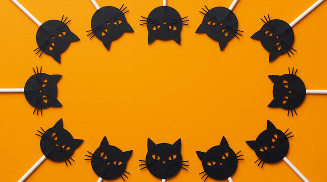Halloween orange background featuring cat face lollipop paper cut out border frame, copy space for spooky party invitation, greeting card, banner, poster, flyer and festive autumn design