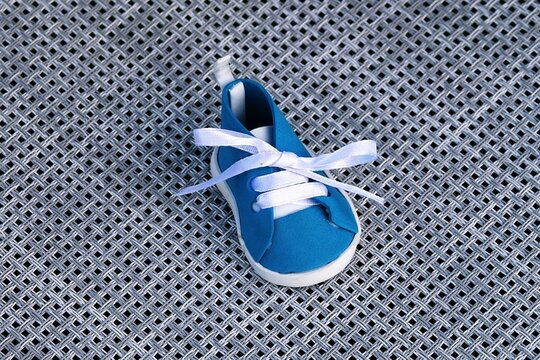 Tiny blue baby sneaker with white laces tied in a bow. A single, small, blue canvas shoe designed for infants, featuring white laces tied neatly into a bow, resting on a textured surface