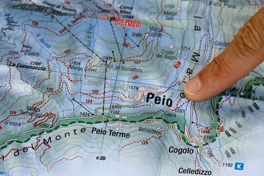 Hand pointing to a topographic map of Stelvio National Park in the Italian Alps. A person's hand indicates a specific location on a detailed topographical map of the mountainous Stelvio National Park 