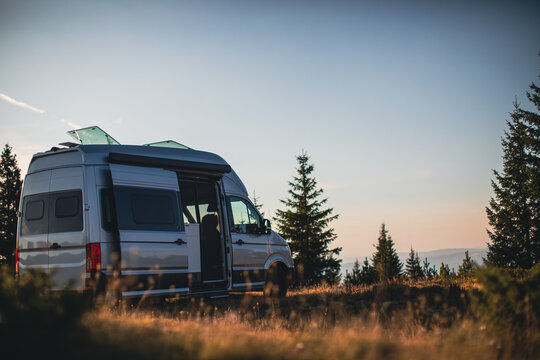 Camper van parked in a peaceful forest clearing during golden hour, showcasing van life and outdoor travel