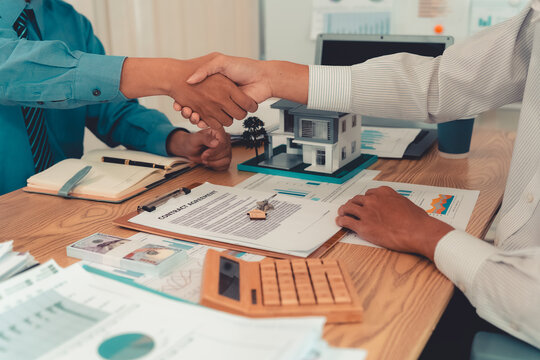 Real estate agent shaking hands with client after signing contract agreement for buying house.