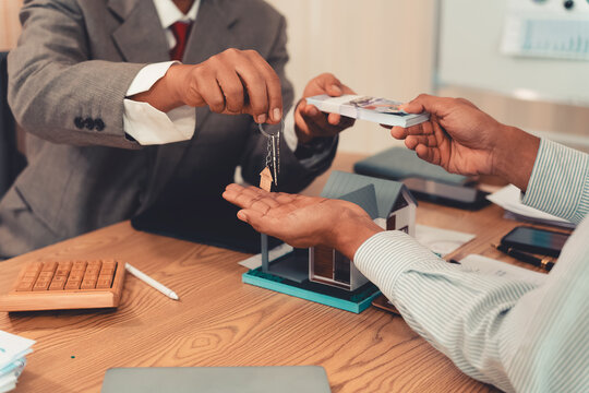 Real estate agent handing over keys to buyer in exchange for cash during house purchase transaction.