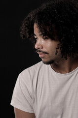 Fototapeta premium Young man with curly hair and a goatee looking down in profile with a pensive expression