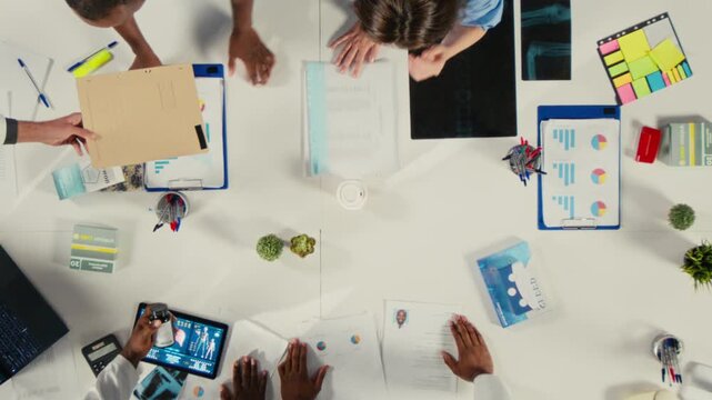 Healthcare professionals discuss therapy options from an overhead angle in a hospital office, using clinical information and treatment notes to support care planning inside a medical team.