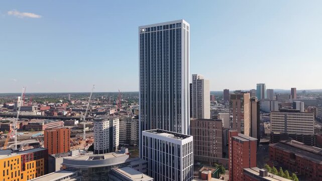 Smooth aerial drone ascent beside a modern skyscraper in Birmingham, England, gradually revealing the city&rsquo;s impressive skyline. As the drone climbs, contemporary high-rise buildings, office towers