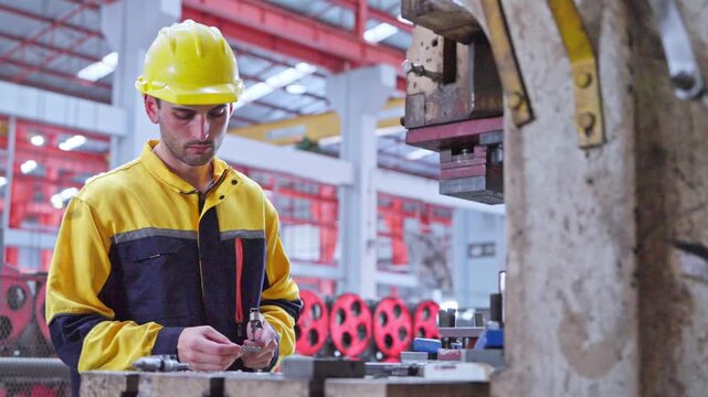 Two experienced professionals working together in a production environment wearing safety helmets and using tools