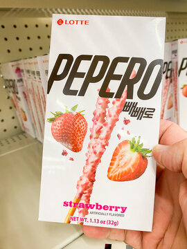 Customer holding a white box of Lotte Pepero Strawberry artificially flavored biscuit sticks.