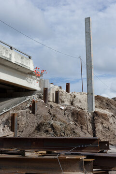 Coastal bridge repair site showing eroded sand embankment, concrete bridge supports, plastic sheeting and construction materials used for stabilization and temporary erosion control during repairs.
