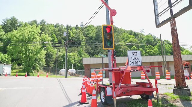 Traffic signal system at a construction site changes from red to green, with orange cones marking the area and a "No Turn on Red" sign clearly visible, alongside green trees and a commercial building