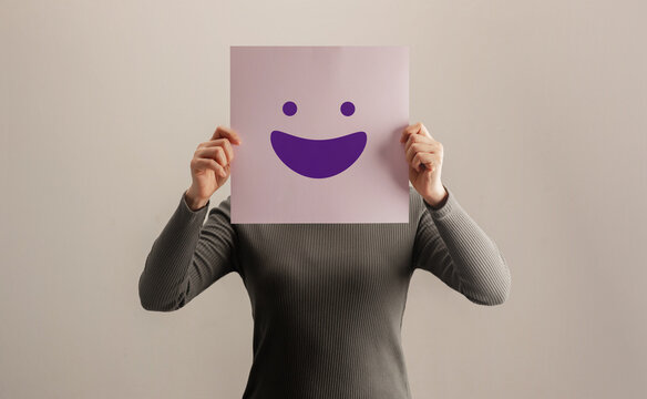 Person covering their face with a smiling paper mask .hidden emotions