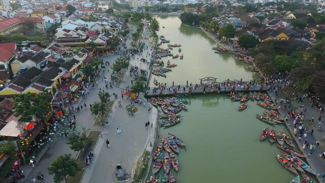 Vertical screen Aerial View Hoi An Crowded Riverfront With Dozens Of Boats And Pedestrians On Bridges, Local Asian Crowds Lining Quays, Bustling Festival Energy, Colorful Hulls And Dense