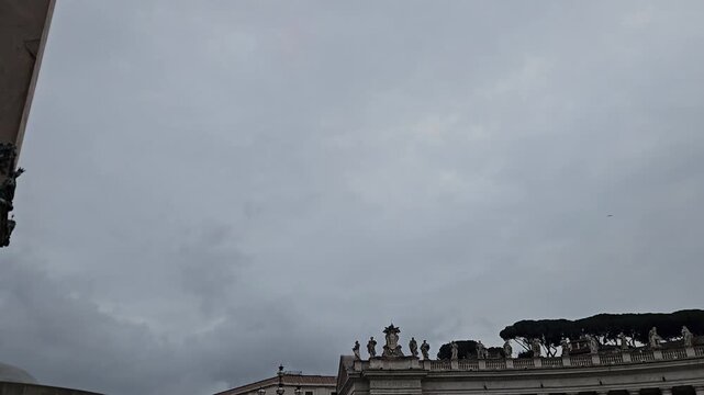 VATICAN CITY - DECEMBER 19, 2025: Low angle panning shot from the Vatican Obelisk to St Peters Basilica facade on an overcast day.