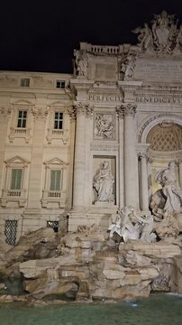 Cinematic vertical view of historic stone sculptures and glowing turquoise pool of Trevi Fountain after sunset. European travel stock footage.