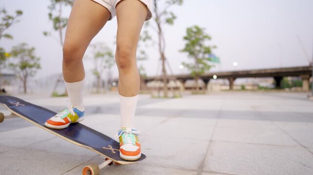 Young Asian woman practicing longboard skateboard on urban public park during late afternoon enjoy active lifestyle outdoor recreation balance fitness freedom healthy leisure and modern city mobility