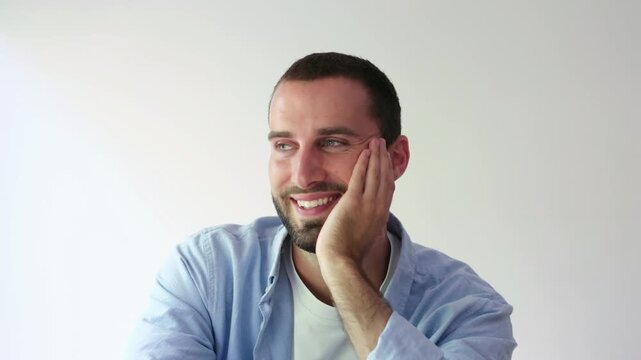 Handsome caucasian man with a beard and blue eyes sits and looks at the camera with a playful and flirtatious expression, smiling and winking while isolated on a white background