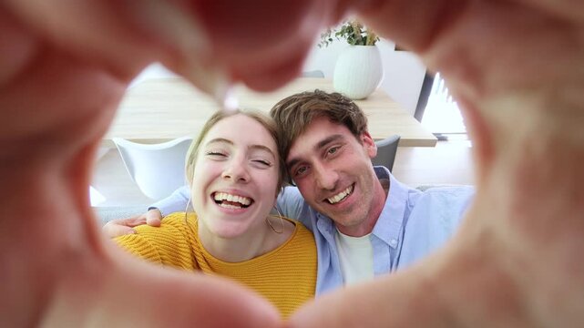 Happy young couple in love showing a heart gesture with their hands while looking at the camera from a personal perspective, symbolizing affection, romance, happiness and positive emotions