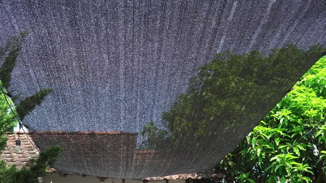 Black Sunshade Net Swaying in the Wind Above a Backyard