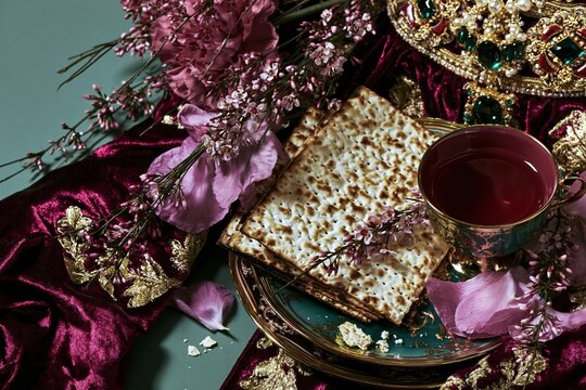 Traditional unleavened matzah bread on a decorative plate with flowers and jewelry for a Jewish Passover Seder celebration, copy space on teal background