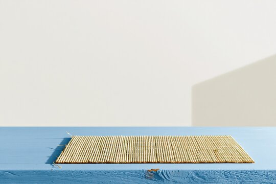 Empty blue wooden table with a bamboo place mat against a white wall, clean rustic kitchen surface for product mockup and food