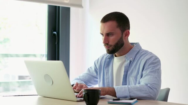Overworked caucasian man feeling tired and frustrated while working on a difficult project at his desk. Young freelancer experiencing professional burnout and headache from overwork