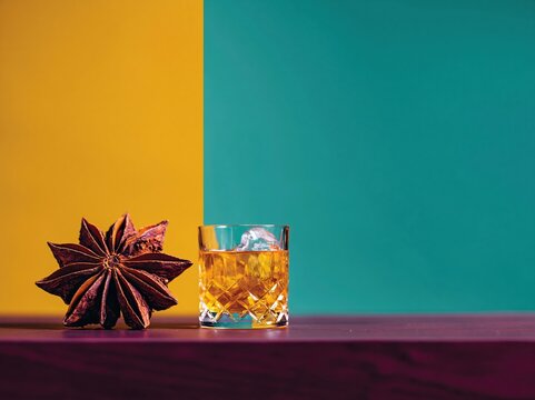 Giant star anise spice beside a crystal tumbler of amber cocktail on a dark wooden surface for autumn drink branding and seasonal spice promotions