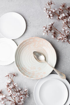 Top view of ceramic plate with a pink cherry blossom pattern, and white side plates on white concrete background, Elegant minimalist table setting concept for food photography, table setting
