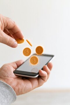 Close-up of a hand holding a smartphone as coins fall onto the screen, representing digital payments and mobile banking