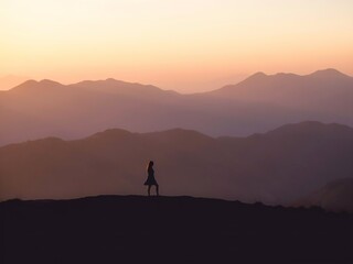 Fototapeta premium Silhouette of a woman standing on a mountain ridge at sunset