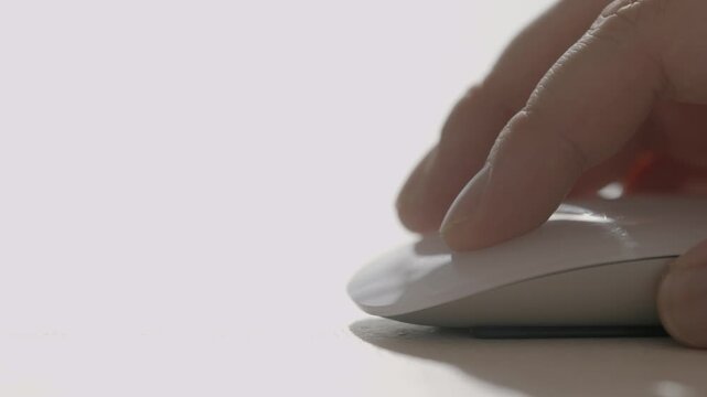 A close-up of a person's hand using a white Apple Magic Mouse on a clean white desk surface.