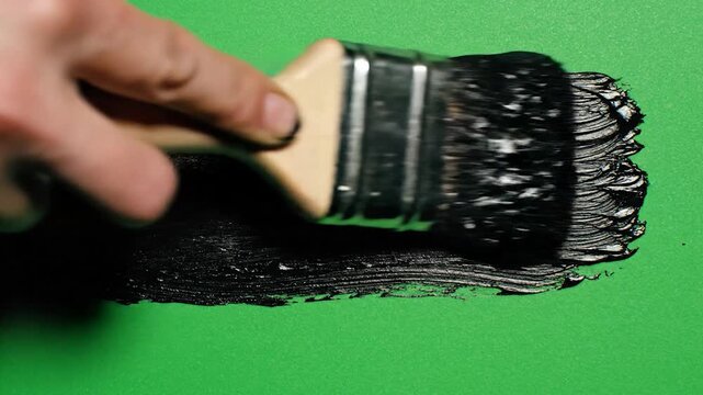A thick black paint stroke sits on a solid green surface