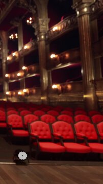 Rows of red seats are ready for the audience in a theater. The lights are dimmed and the stage is set for an upcoming show later in the evening.