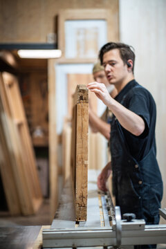 Professional master restorer evaluating and examining condition of antique wooden door before restoration in carpentry studio, thoughtful man woodworker checking and discussing stages for renovation.