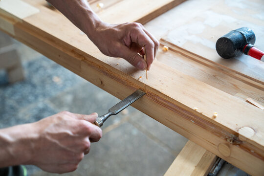 Process of manual woodworking in restoration workshop, carpenter working with chisel hand tool, professional craftsman holding instrument and cutting surface in wooden board, handwork reconstruction.