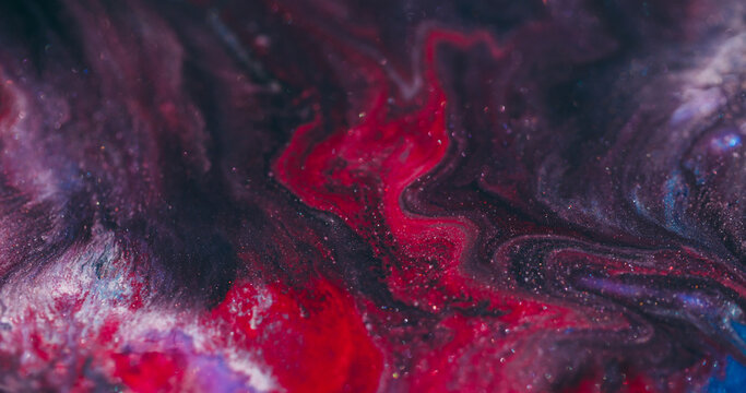Shimmering acrylic. Art fluid blur. Red paint wavy lava stream swirling in black sparkling liquid on abstract color flare background.