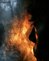 Obraz premium Silhouette shows rain droplets outside the window. Firelight creates warmth inside, highlighting contrast and resilience against struggles.