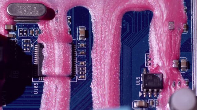 Chip scheme. Ink trickles. Shimmering pink fluid pouring on blue motherboard texture. Color electronics system defocused background.
