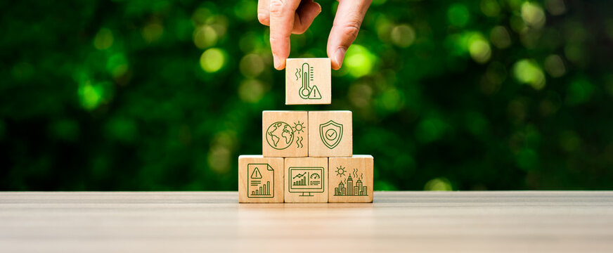 Climate risk management concept with hand placing heat warning icon cube on wooden pyramid blocks showing global warming impact urban safety environmental protection and sustainability planning