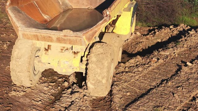 Heavy yellow dumper truck reversing slowly in the mud