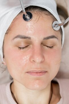 Woman face. Microcurrent stimulation. Professional esthetician performing lifting procedure using modern device in beauty salon.