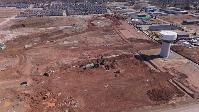 Drone video shows a wide, dusty construction site in Erin, Ontario, with heavy machinery, new housing plots, and the Erin water tower under bright daylight. Modern development, aerial footage.