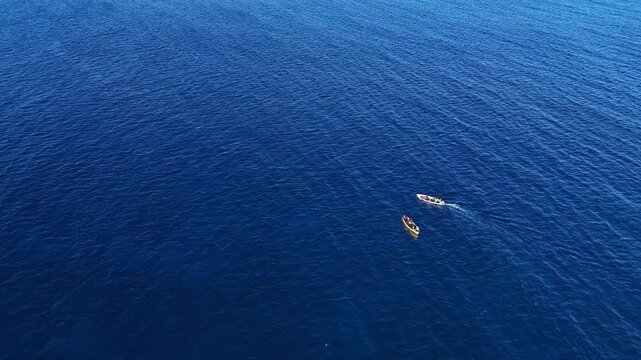 Pair of small traditional fishing boats cruise in clear blue tropical sea. Drone