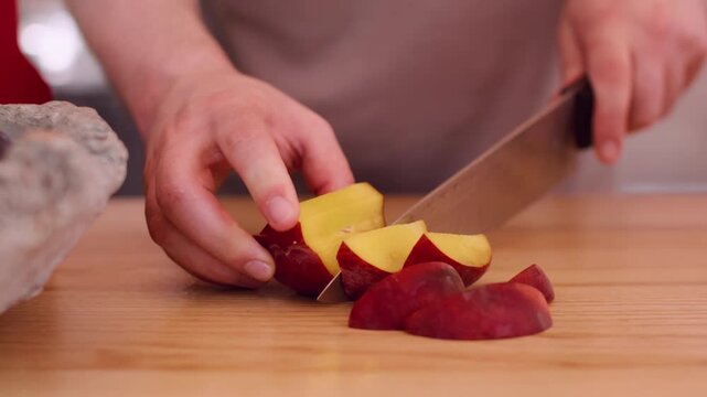 Ripe nectarine slicing. Fruit preparing. Unrecognizable man chef hands using sharp knife on wooden board making peeling snack at workspace.