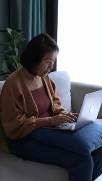 Asian mature woman typing on keyboard laptop working from home