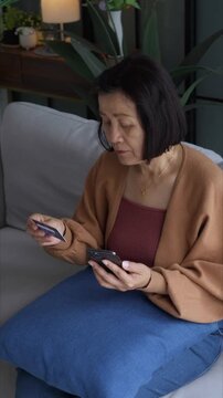 Asian mature woman using credit card booking ticket online on smartphone