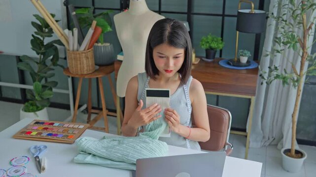 Asian woman tailor showing cloth texture example to customer on laptop